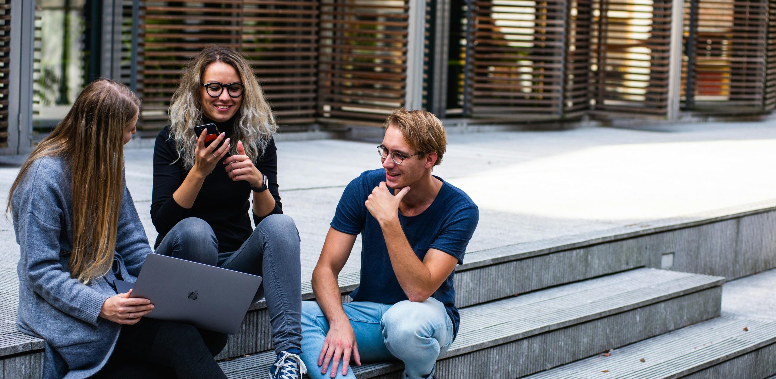 Three young professionals having a friendly chat while sitting on outdoor steps.