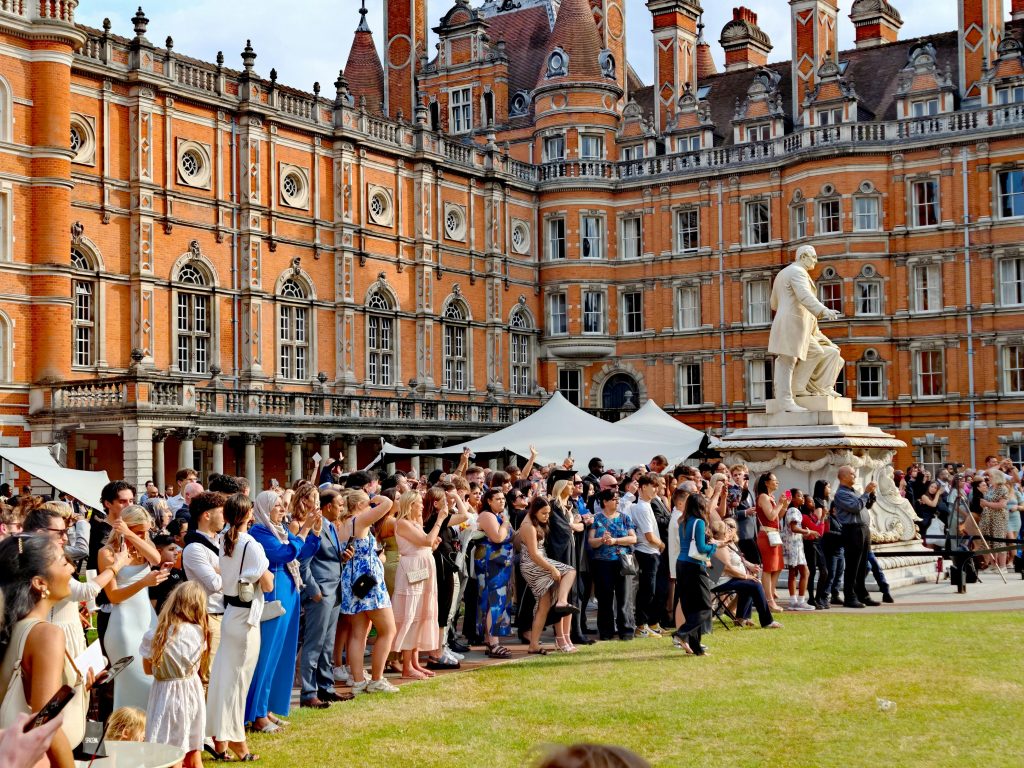 A large crowd gathers for a graduation ceremony at a historic university in England, featuring ornate architecture.