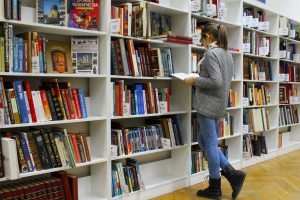 A young woman stands reading a book in a well-stocked library.